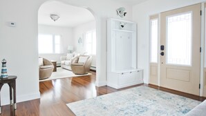 Amplia sala de estar con piso de madera, un tapete grande, un armario blanco y una puerta con paneles de vidrio.