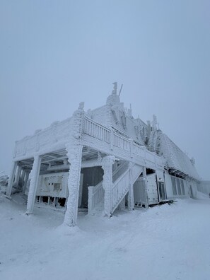 A snow-covered building with a balcony and a staircase leading to the entrance.