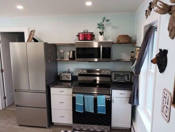 A compact kitchen with a refrigerator, microwave, toaster, oven, and a small countertop with a plant.