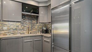 Eine moderne Küche mit einem Edelstahlkühlschrank, grauen Schränken und einer Mosaik-Spritzschutzleiste.