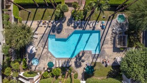 Eine Vogelperspektive zeigt ein Resort mit Schwimmbecken, Liegestühlen und Palmen.