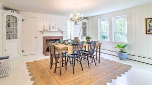 A dining area with a wooden table, chairs, and a chandelier. There is a fireplace and a potted plant. - Steps to Dennis Village! 'The Blue Scallop' Home (Dennis)