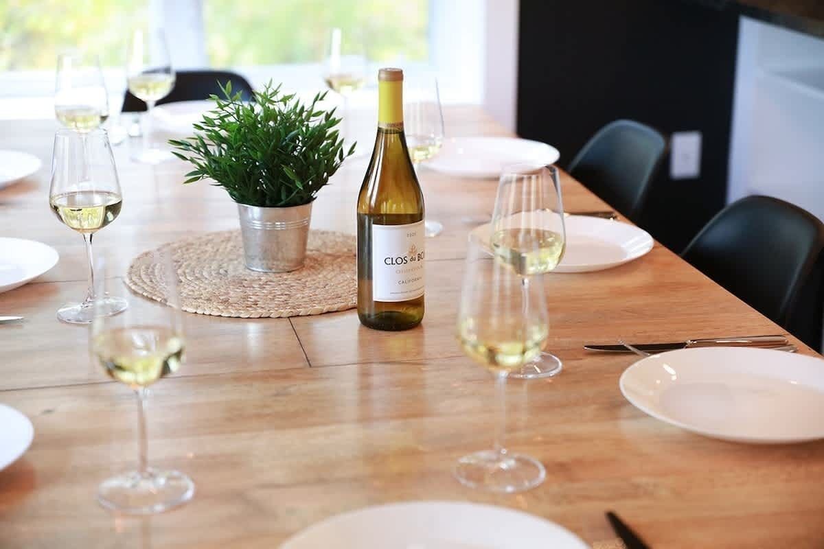 Une table à manger dressée avec de l’assiette blanche, des verres à vin et une bouteille de vin.