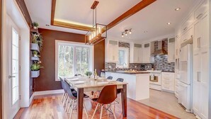Una cocina moderna con armarios blancos, una isla central y un comedor con mesa y sillas de madera.