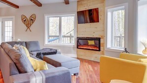 Una sala de estar moderna con chimenea, vigas de madera y ventanas amplias.