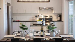 Una cocina moderna con armarios blancos, una campana extractora de acero inoxidable y un comedor con mesa para cuatro.