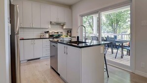 Una cocina moderna con armarios blancos, encimera negra y un ventanal con vistas a una terraza.