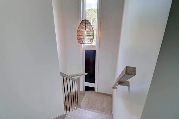 Eine Treppe mit Holzwurf und einer weißen Wand, darüber eine Pendelleuchte.