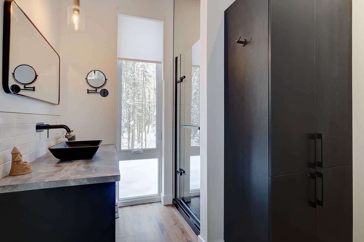 Un bany modern amb un mirall gran, un lavabo negre i una porta de banyera de vidre.