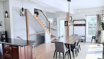 A modern kitchen with a wooden island, a dining area with a long table and chairs, and a staircase with a railing.