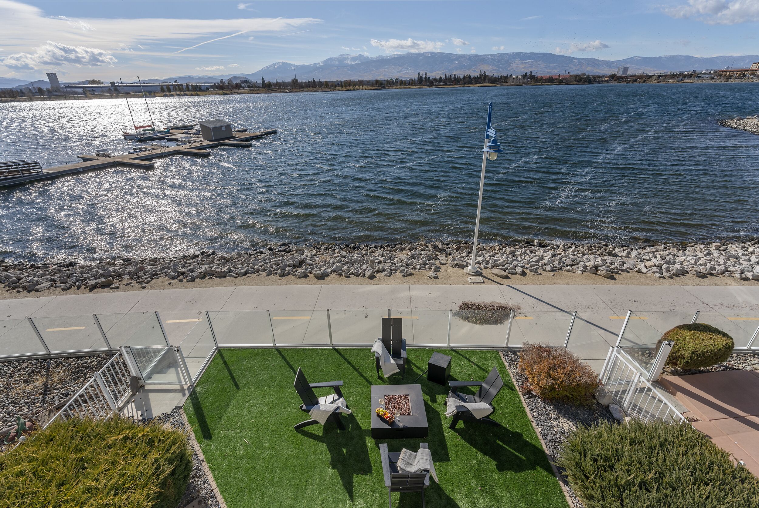 A patio with outdoor furniture overlooking a lake, a dock, and mountains in the background.