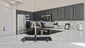 Une cuisine moderne avec des meubles de couleur sombre, des appareils électroménagers en acier inoxydable et un plan de travail en marbre.
