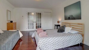 Un dormitorio con dos camas, cabeceros de madera, un cuadro en la pared y una puerta con paneles de vidrio esmerilado.