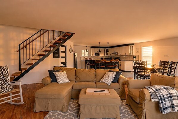 A living room with a sofa set, ottoman, and a staircase.