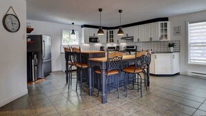 Una cocina moderna con armarios blancos, una isla central con taburetes, iluminación colgante y un reloj en la pared.