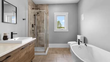 Une salle de bain moderne avec une douche à parois de verre, une grande baignoire et une fenêtre donnant sur la verdure.