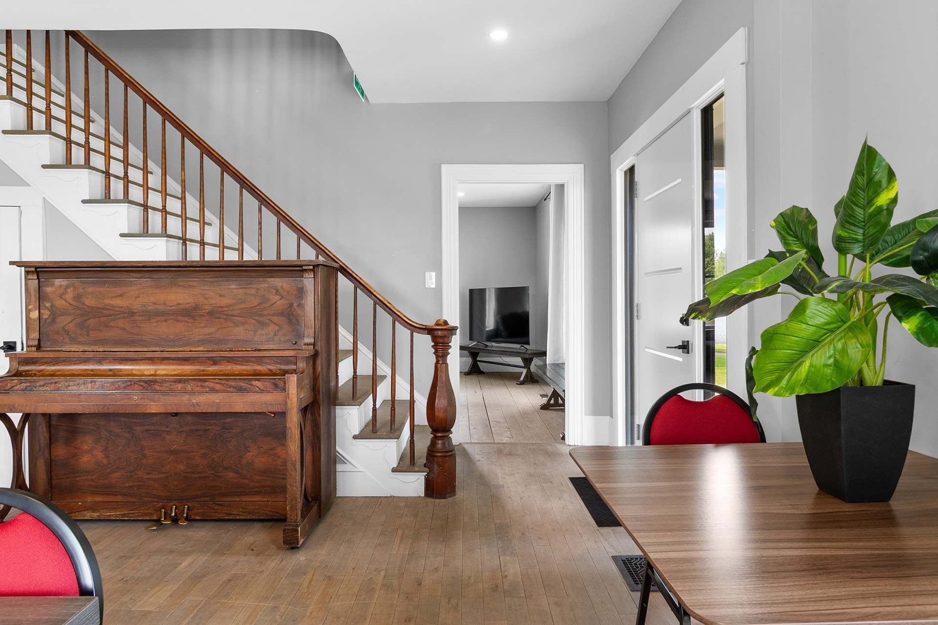 A modern interior with a wooden staircase, a dining area with a table and chairs, and a large potted plant.