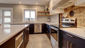 A modern kitchen with a large island, built-in oven, and a brick accent wall.