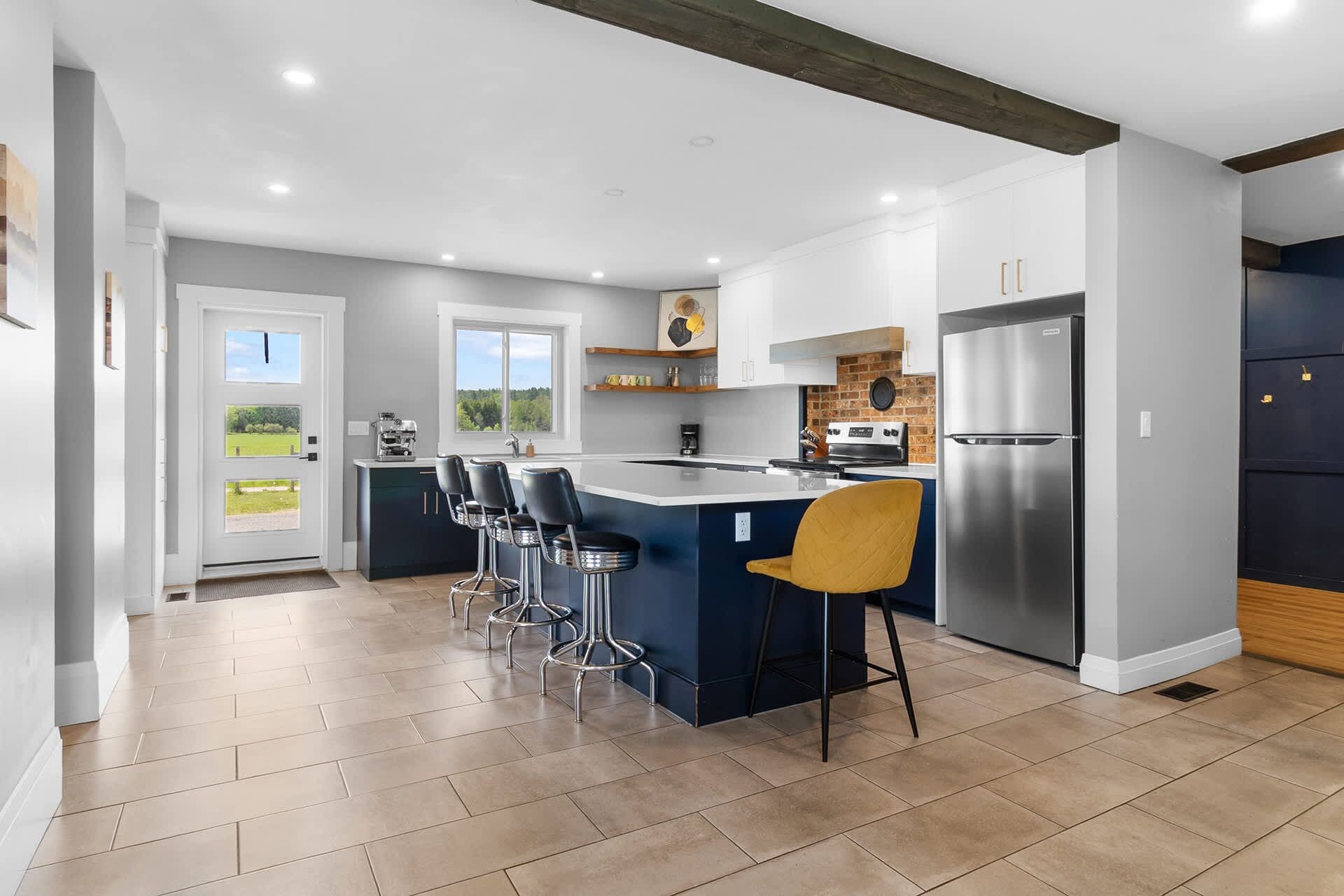 Una cocina moderna con una isla central, taburetes de bar, un refrigerador y vistas al exterior.