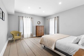 A bedroom with a bed, a wooden dresser, a wicker chair, and a mirror on the wall.
