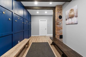 A hallway with blue lockers, a wooden bench, a door, and a brick wall with a painting.