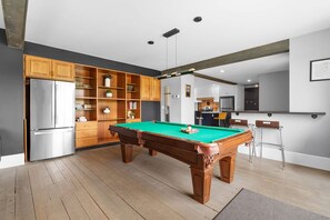 Una cocina moderna con mesa de billar integrada, armarios de madera y refrigerador.