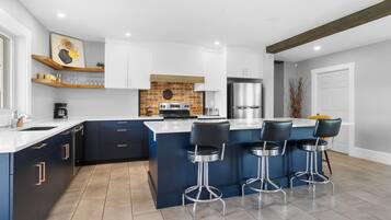 A modern kitchen with a central island, bar stools, and a brick accent wall.