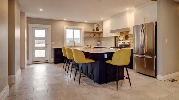 A modern kitchen with a central island, bar stools, a stainless steel refrigerator, and a window providing natural light.