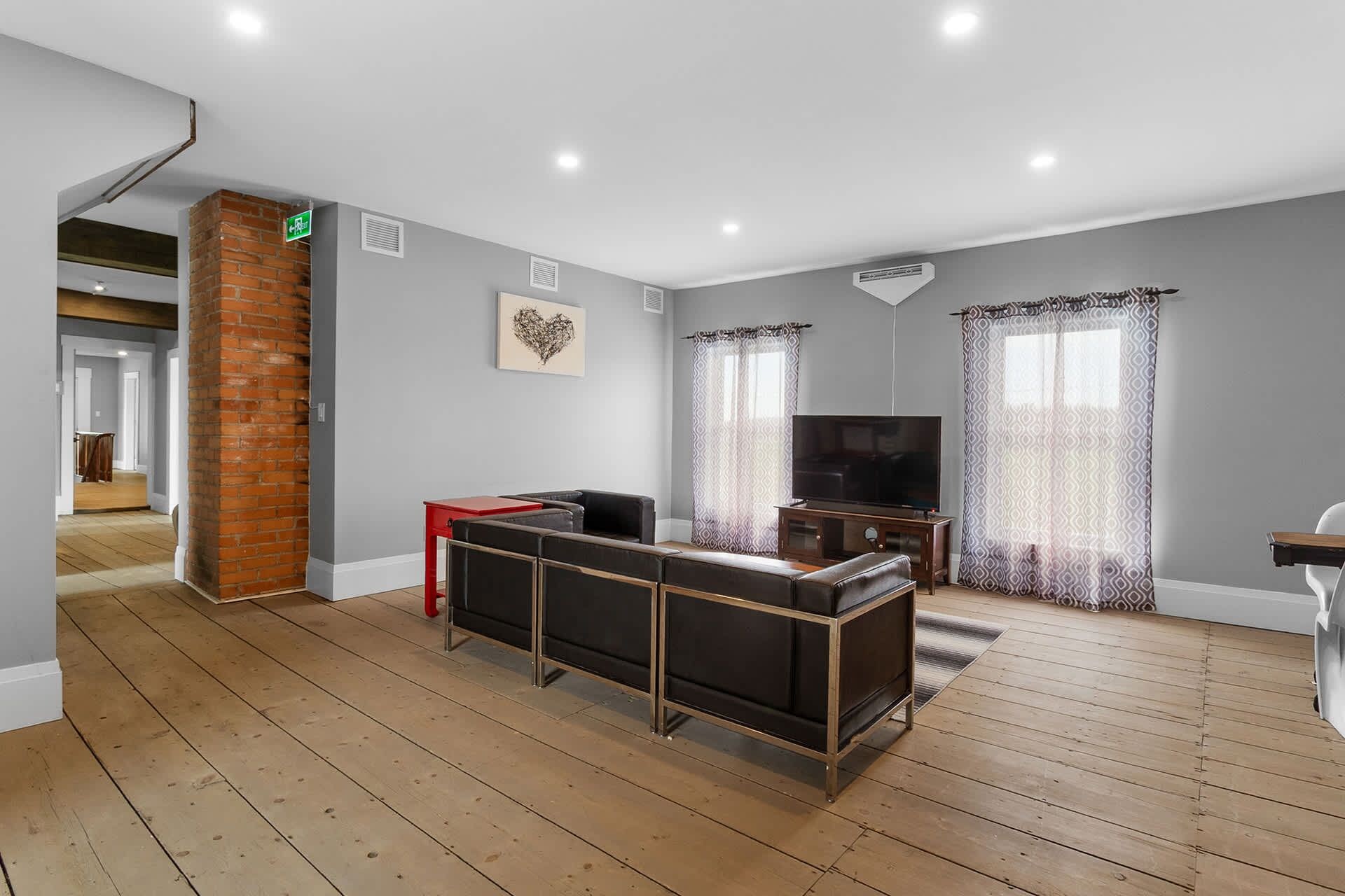 Une pièce spacieuse avec un plancher en bois, un mur décoratif en briques, un téléviseur à écran plat et un canapé.