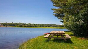 A wooden picnic table by a calm lake with a clear sky.