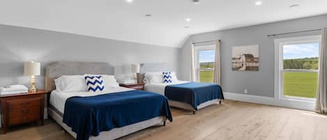 A bedroom with two beds, a wooden floor, and a large window with a view of a field.