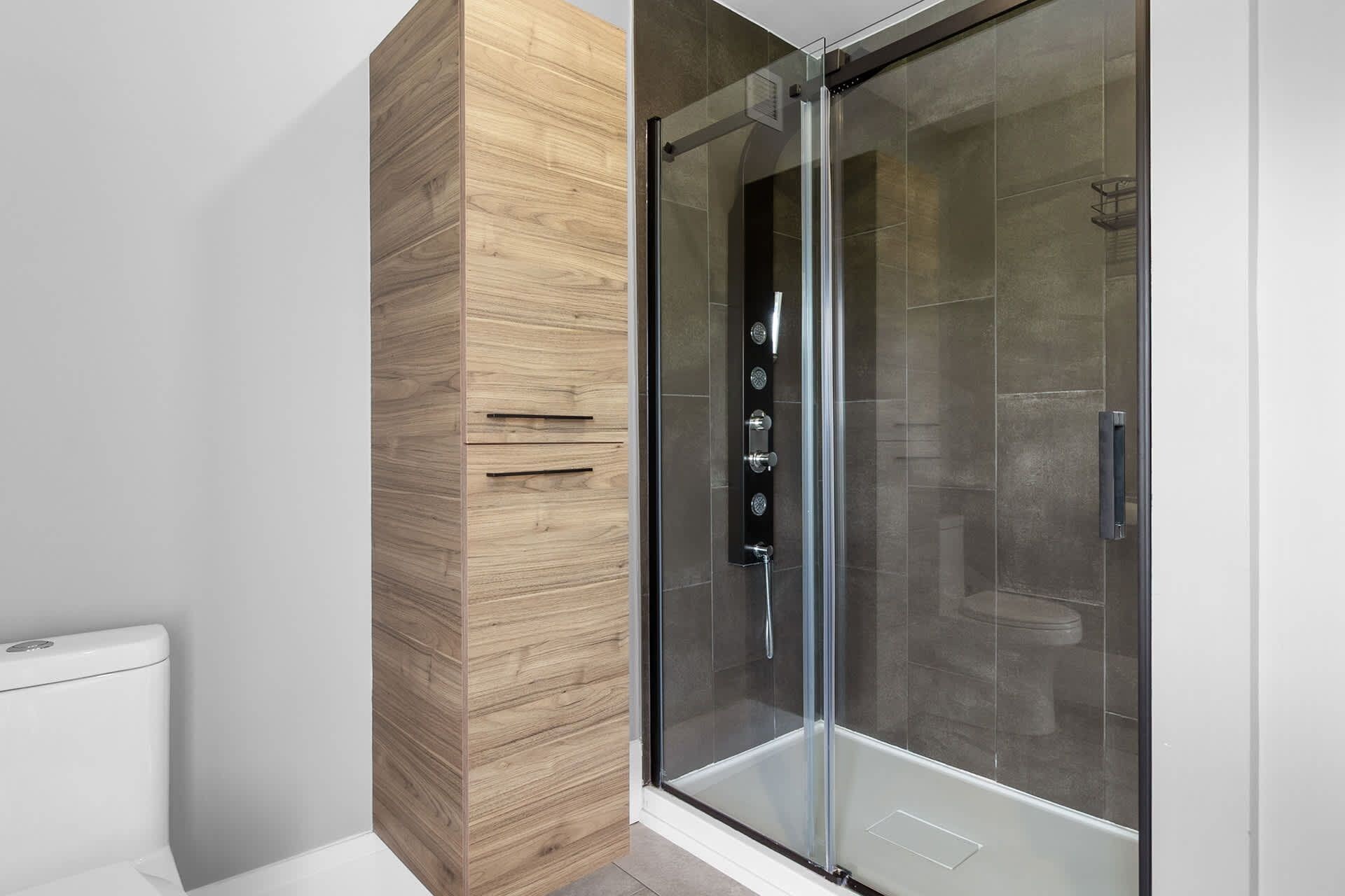 Ein modernes Badezimmer mit einer in Glas abgeschlossenen Dusche, einem Holzbadezimmermöbel und einer weißen Toilette.
