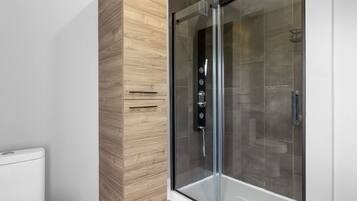 Ein modernes Badezimmer mit einer in Glas abgeschlossenen Dusche, einem Holzbadezimmermöbel und einer weißen Toilette.
