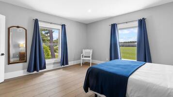 A bedroom with a bed, a chair, and two windows with curtains.