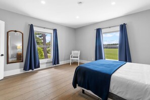 Una camera da letto con un letto, una sedia e due finestre con tende.