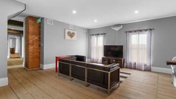 A spacious room with a wooden floor, a brick accent wall, a flat-screen TV, and a sofa.