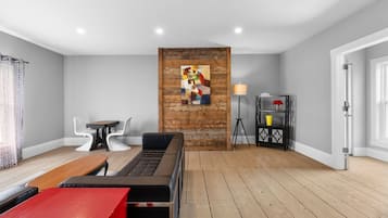Un salon moderne avec un mur d’accent en bois, un canapé rouge, un canapé en cuir noir, une table à manger et un lampadaire.