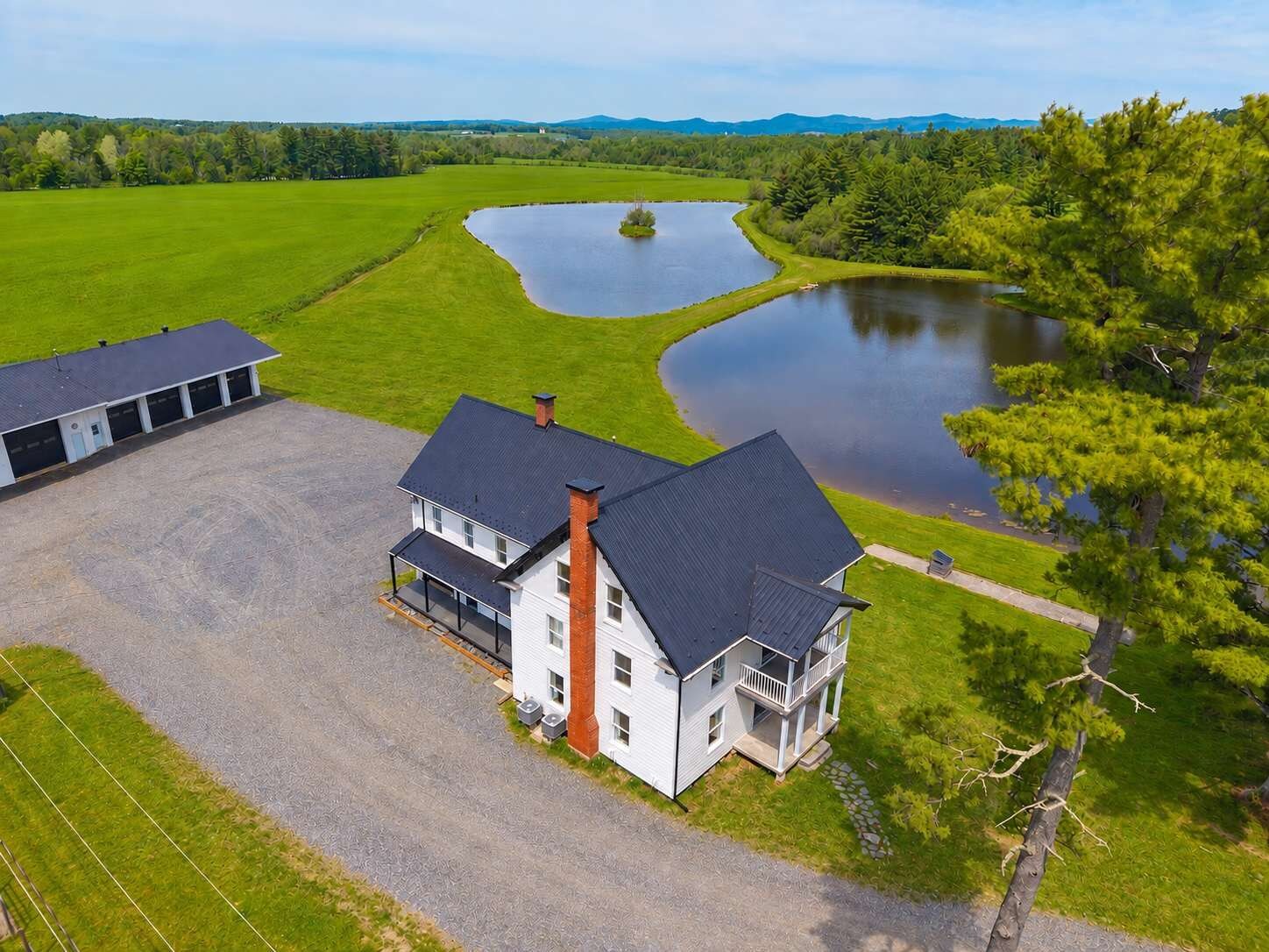 A two-story house with a large driveway and a pond in the background.