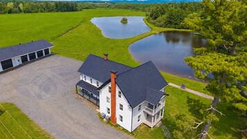 A two-story house with a large driveway and a pond in the background.