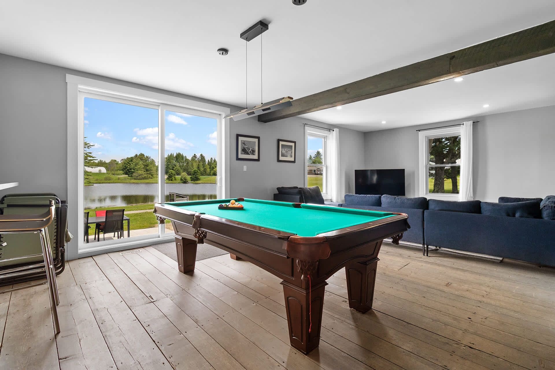 A pool table in a room with a large window, a sofa, and a television.