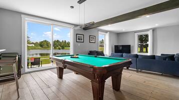 A pool table in a room with a large window, a sofa, and a television.