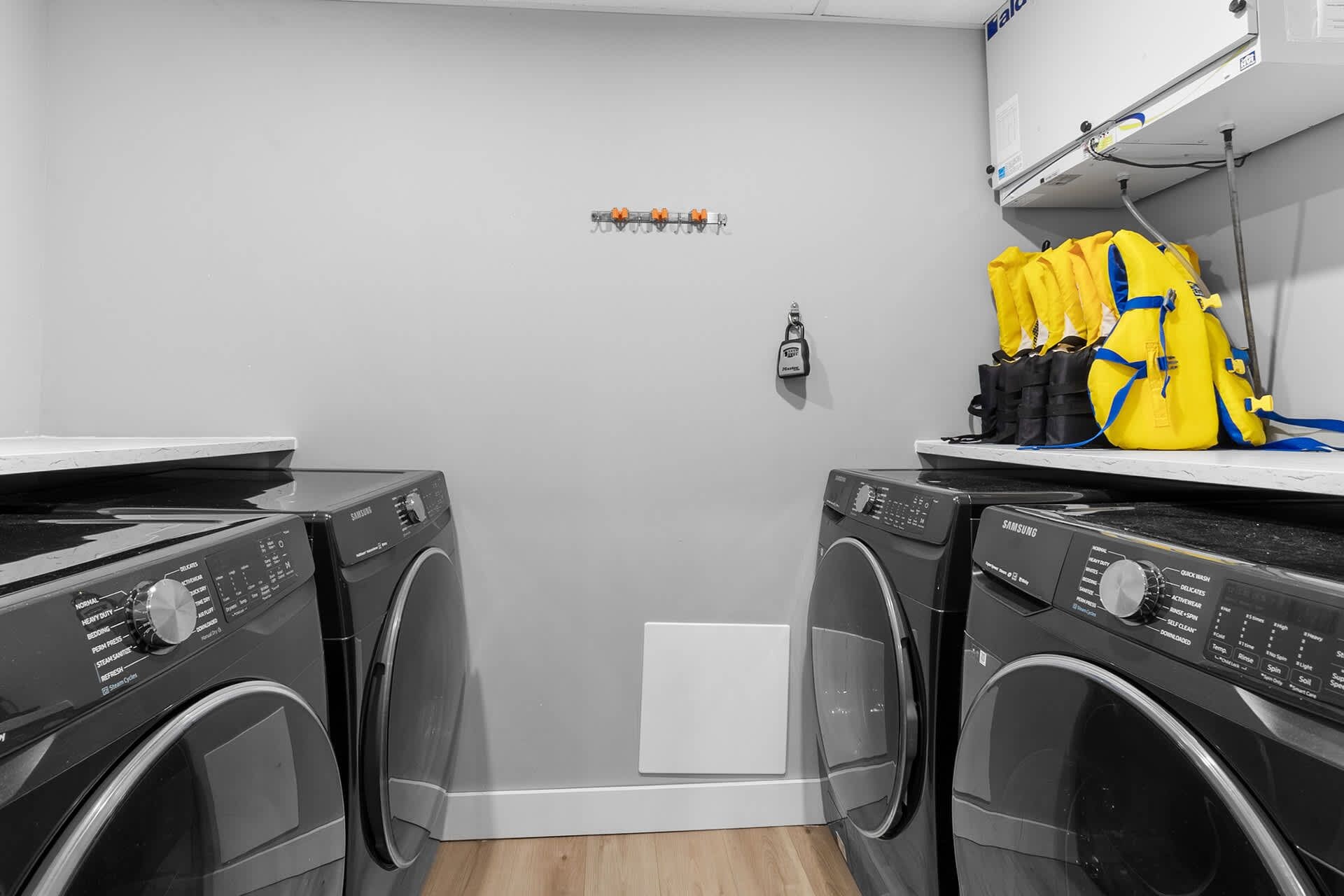 A laundry room with two front-loading washing machines, a small white cabinet, and a yellow backpack on a shelf.