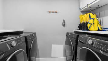 A laundry room with two front-loading washing machines, a small white cabinet, and a yellow backpack on a shelf.