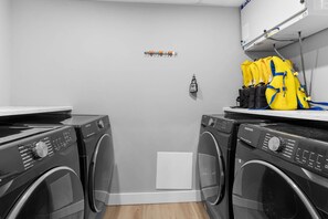 A laundry room with two front-loading washing machines, a small white cabinet, and a yellow backpack on a shelf.