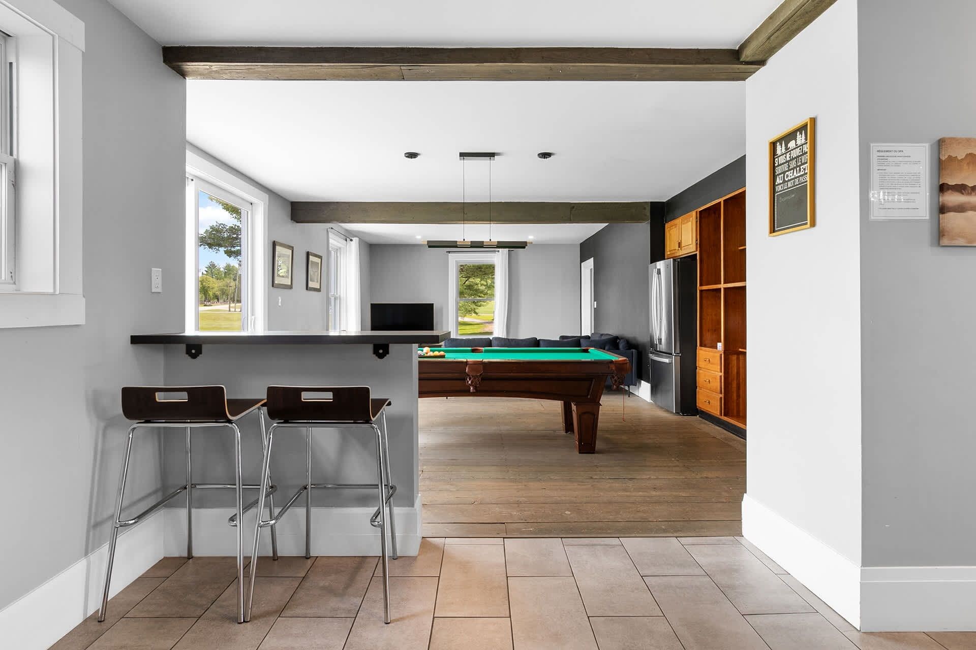 A modern kitchen with a pool table, bar stools, and a view of the outdoors.