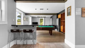 A modern kitchen with a pool table, bar stools, and a view of the outdoors.