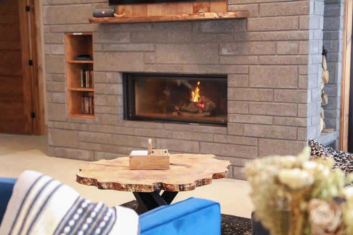 A living room with a stone fireplace, a round wooden coffee table, and a bookshelf.