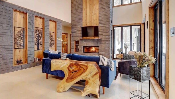 A modern living room with a fireplace, blue sofas, and a unique wooden coffee table. - Mont Owl's Head - Sauna - Spa - Inground Pool (Mansonville)