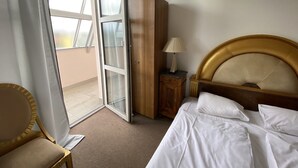 Een hotelkamer met een bed, nachtkastje, lamp, stoel en een glazen schuifdeur die leidt naar een balkon.