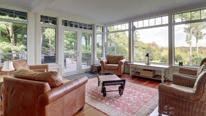 A spacious living room with large windows, leather sofas, a coffee table, and wicker chairs. - Brome Lake - Inground Pool - Spa - Lumen (Knowlton)